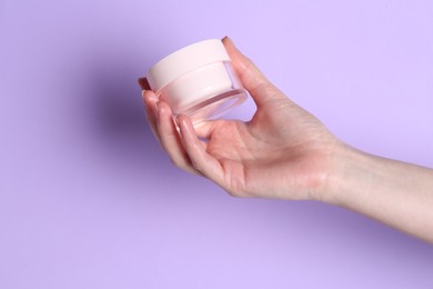 Woman holding jar of cream on violet background, closeup