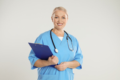 Photo of Mature doctor with clipboard on light grey background