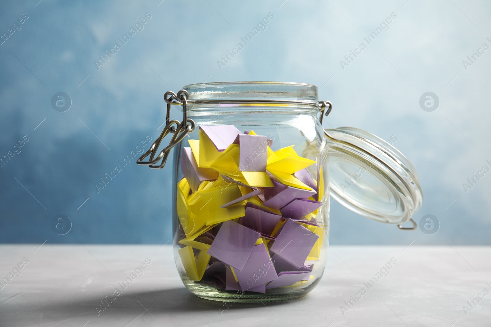 Photo of Colorful paper pieces for lottery in glass jar on color background