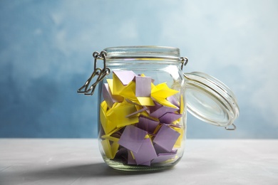 Photo of Colorful paper pieces for lottery in glass jar on color background