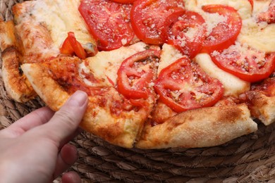 Photo of Woman taking piece of delicious Caprese pizza at table, closeup