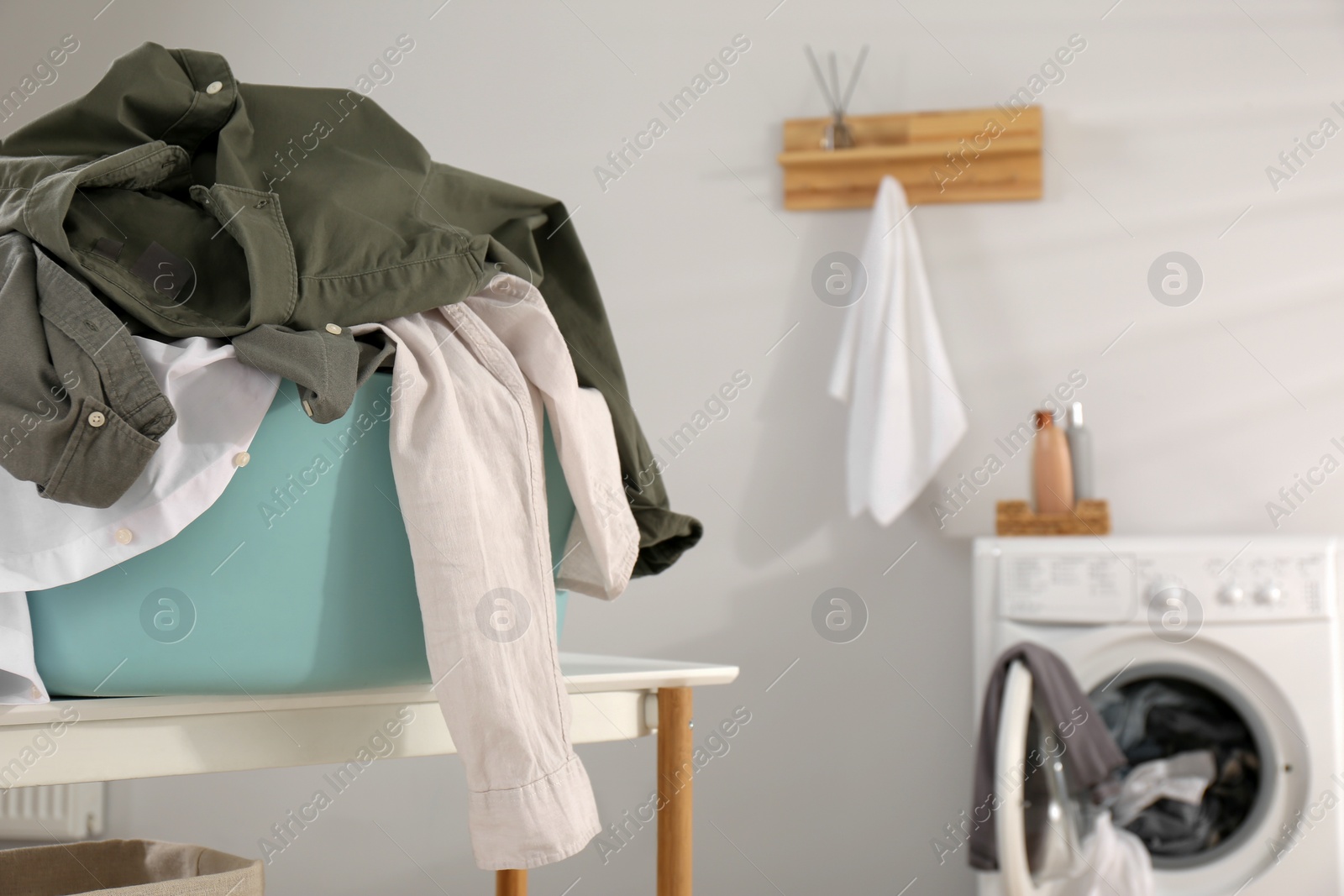 Photo of Laundry basket with clothes on white table near washing machine indoors