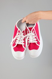 Woman holding pair of classic old school sneakers on light grey background, closeup