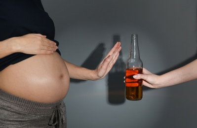 Photo of Pregnant woman declining whiskey on dark background. Alcohol harm