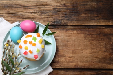 Photo of Easter cake and painted eggs on wooden table, flat lay. Space for text