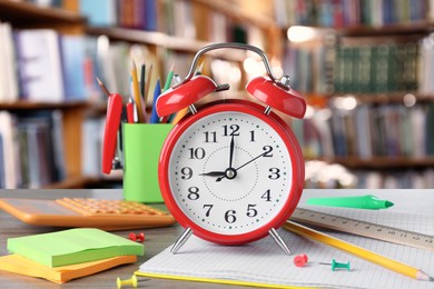 Image of Red alarm clock and different stationery on wooden table in library