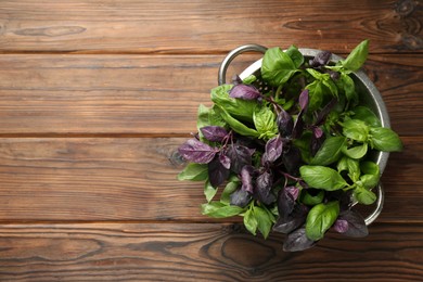 Photo of Metal colander with different fresh basil leaves on wooden table, top view. Space for text