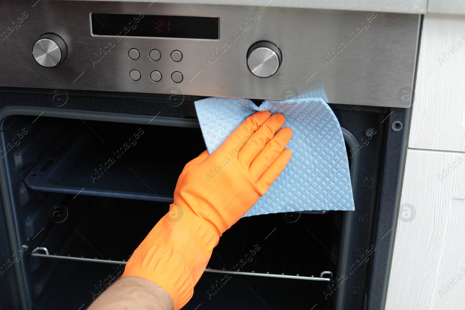 Photo of Young man cleaning oven with rag in kitchen, closeup