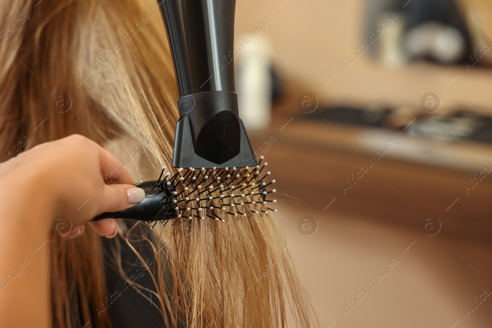 Photo of Professional hairdresser drying girl's hair in beauty salon, closeup