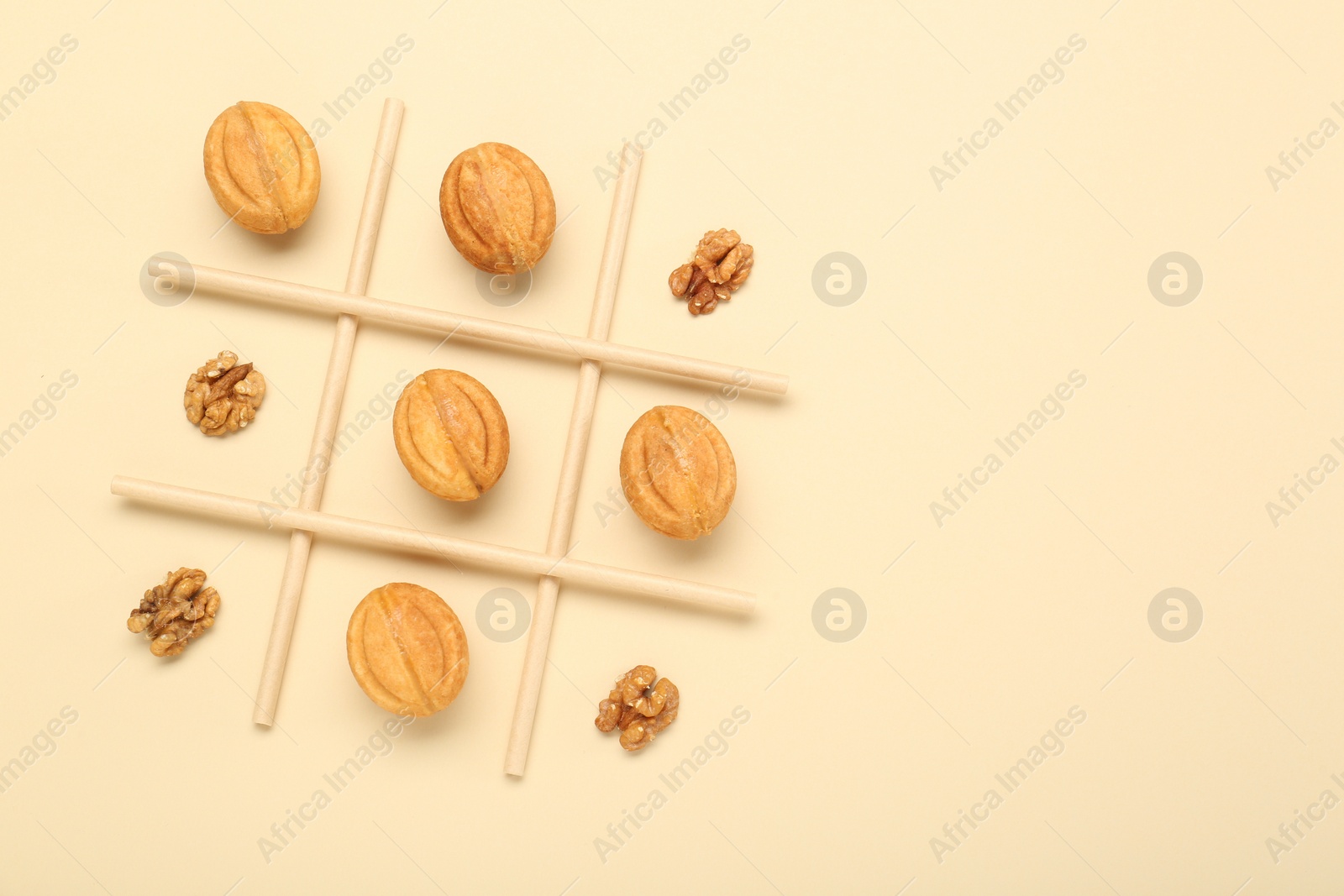 Photo of Tic tac toe game made with walnuts and cookies on beige background, top view. Space for text