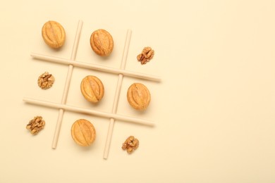 Photo of Tic tac toe game made with walnuts and cookies on beige background, top view. Space for text
