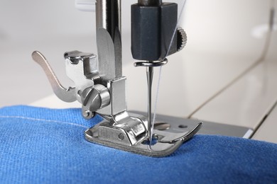 Modern sewing machine with blue cloth, closeup