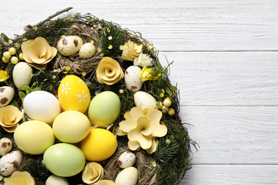 Photo of Decorative wreath with Easter eggs on white wooden background, top view
