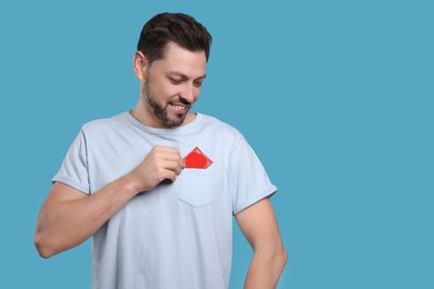 Photo of Smiling man putting condom in his pocket on light blue background. Space for text