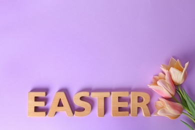 Spring flowers and word EASTER made of wooden letters on color background, top view. Space for text