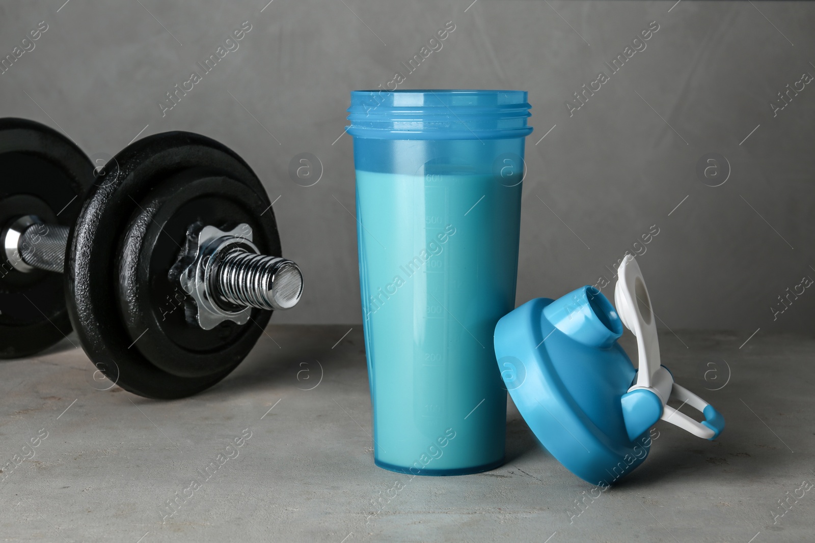 Photo of Bottle with protein shake and dumbbell on grey table