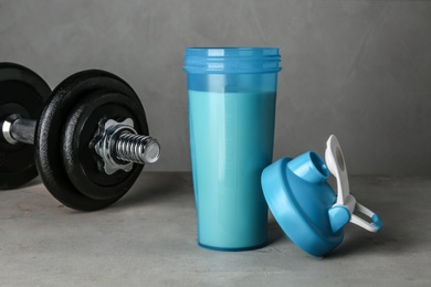 Photo of Bottle with protein shake and dumbbell on grey table