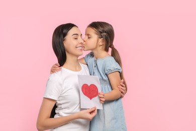 Happy woman with her cute daughter and handmade greeting card on pink background, space for text. Mother's day celebration