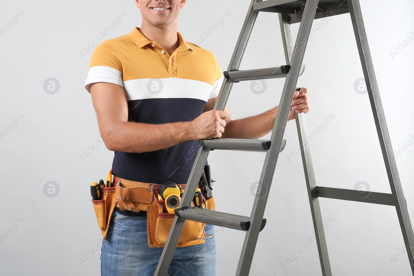 Photo of Professional builder with metal ladder on grey background, closeup