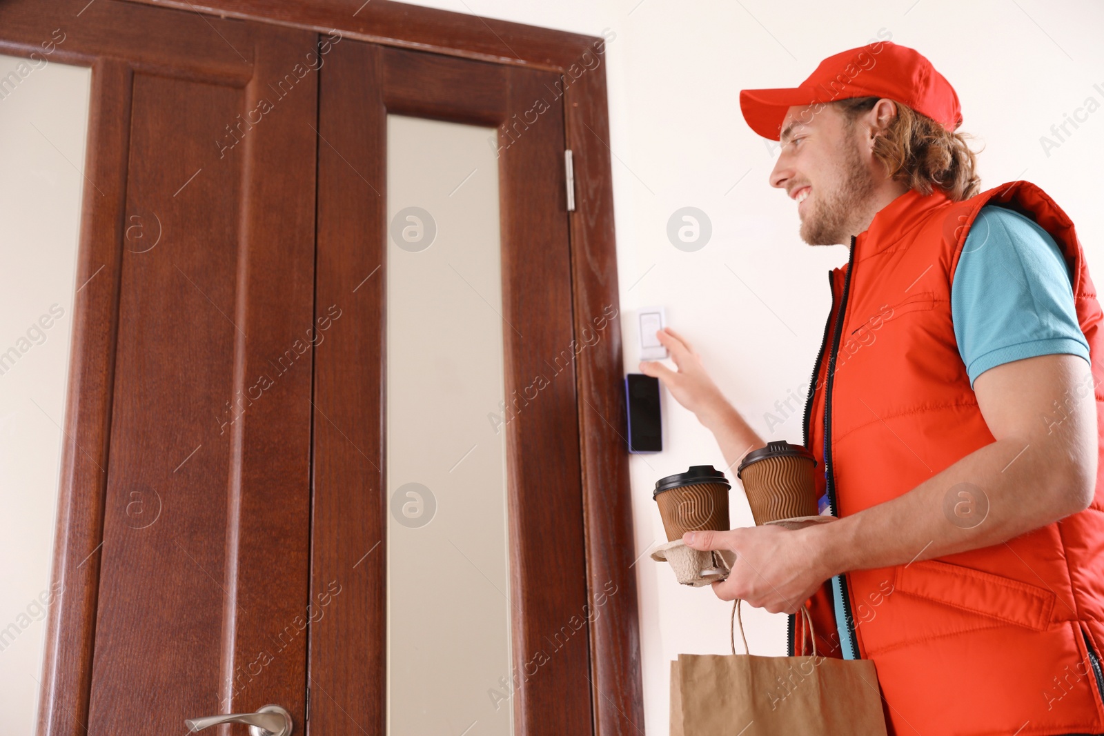 Photo of Male courier with order ringing in doorbell at entrance. Food delivery service