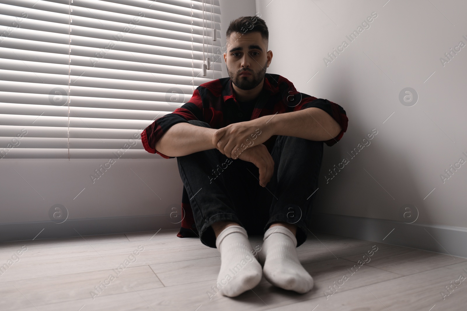 Photo of Sad man sitting on floor at home, low angle view