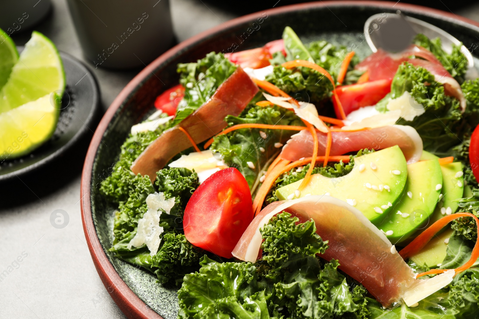 Photo of Delicious kale salad with prosciutto served on grey table, closeup