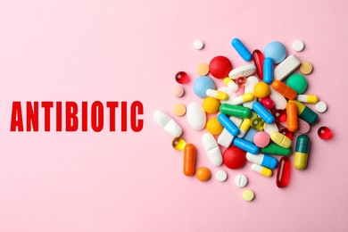 Word Antibiotic and pile of different pills on pink background, top view