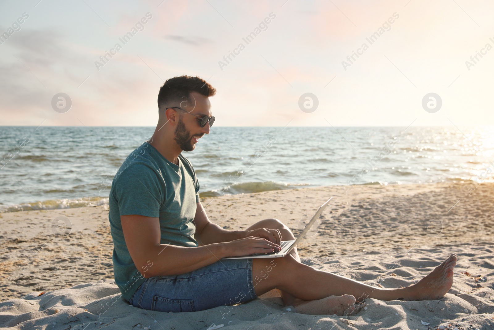 Photo of Man working with modern laptop on beach