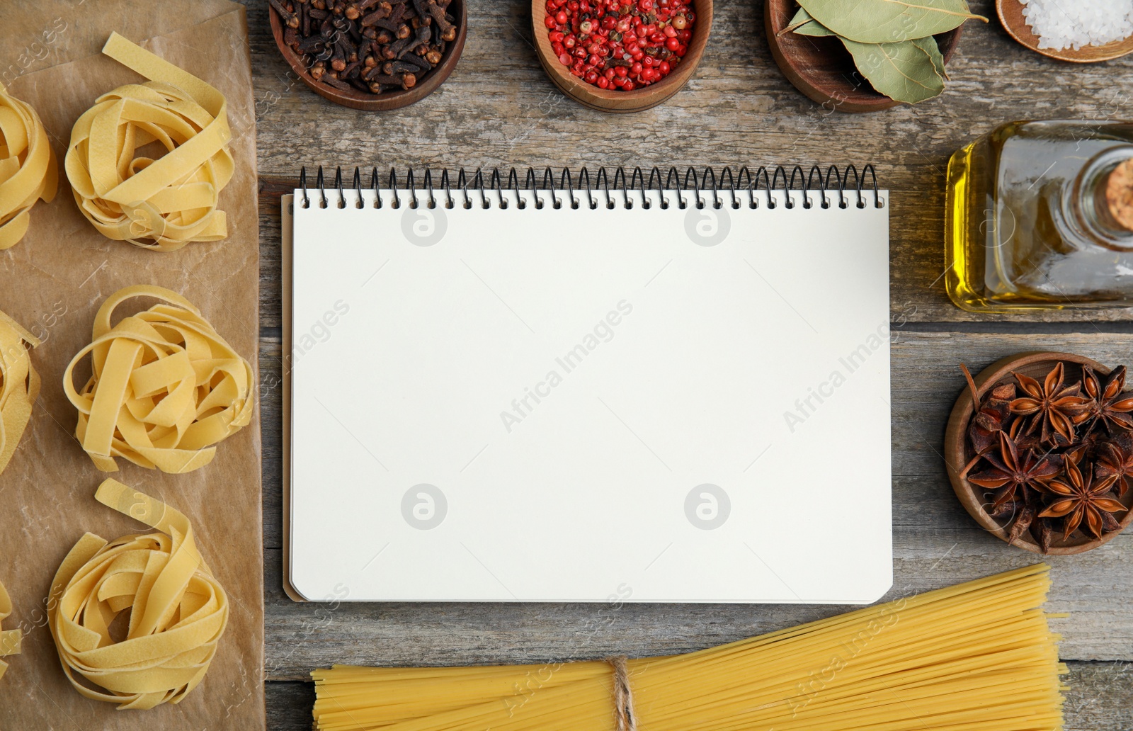 Photo of Blank recipe book, spices and raw pasta on wooden table, flat lay. Space for text