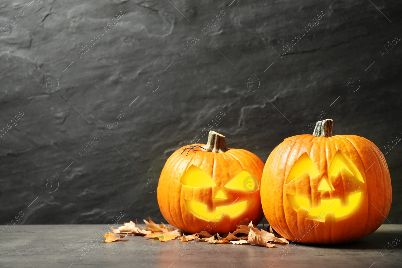 Photo of Scary jack o'lantern pumpkins and fallen leaves on black background, space for text. Halloween decor