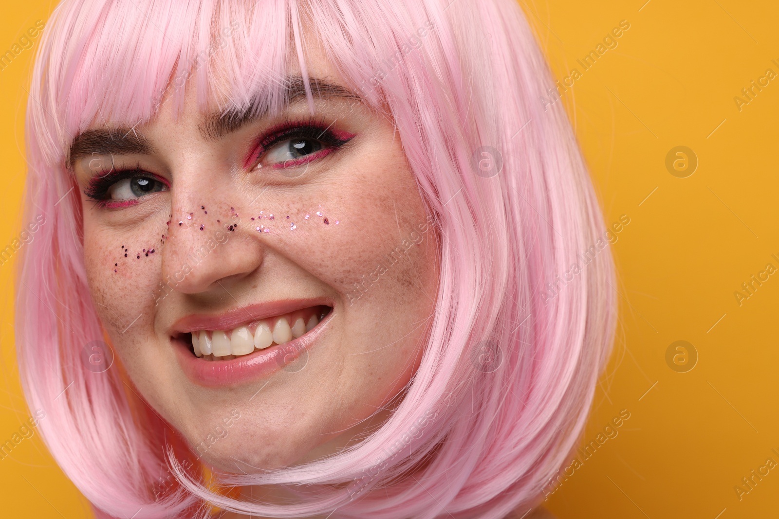 Photo of Smiling woman with bright makeup and glitter freckles on yellow background, closeup