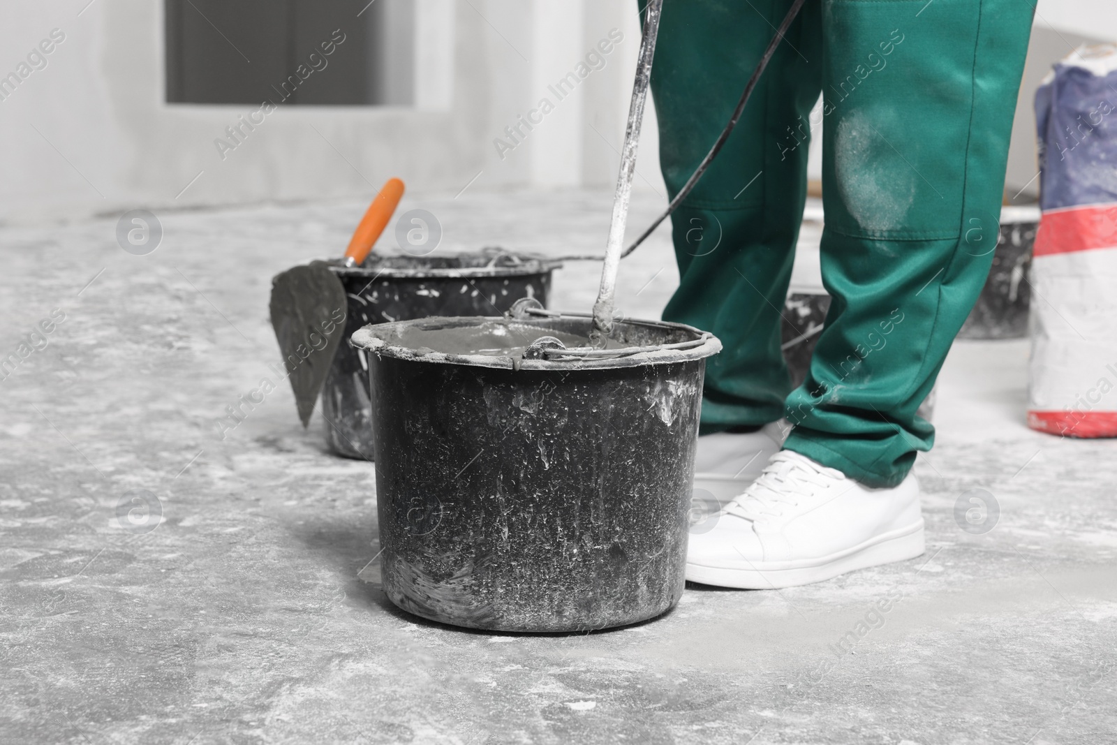 Photo of Worker mixing concrete in bucket indoors, closeup