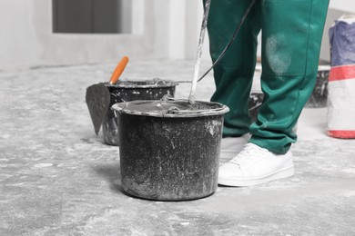 Worker mixing concrete in bucket indoors, closeup