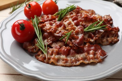 Photo of Slices of tasty fried bacon with rosemary and tomatoes on wooden table, closeup