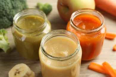 Tasty baby food in jars and ingredients on light wooden table, closeup