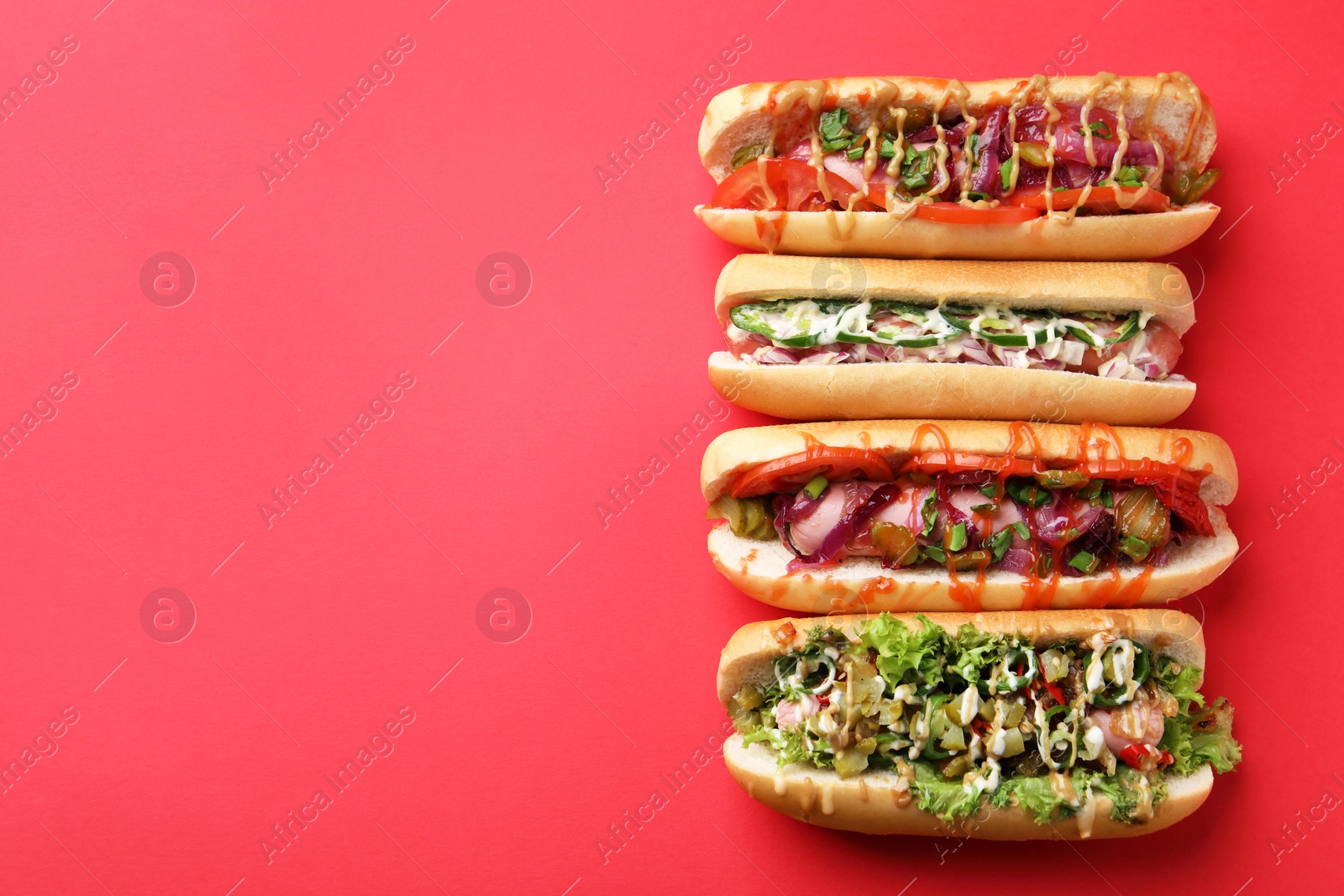 Photo of Delicious hot dogs with different toppings on red background, flat lay. Space for text