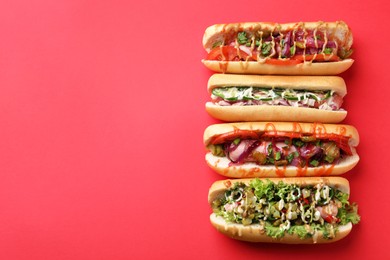 Photo of Delicious hot dogs with different toppings on red background, flat lay. Space for text