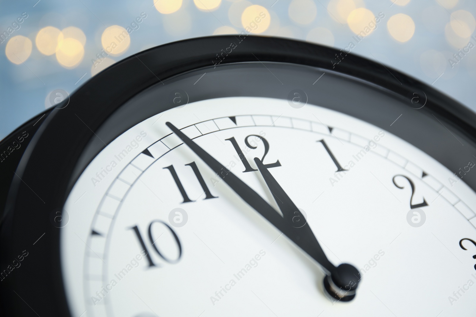 Photo of Clock on light blue background with blurred lights, closeup. New Year countdown