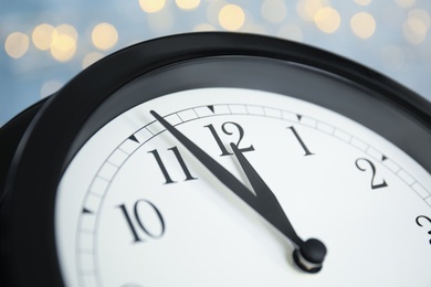 Clock on light blue background with blurred lights, closeup. New Year countdown