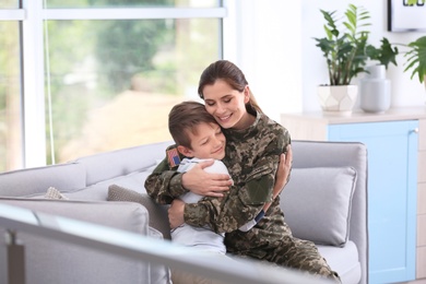 Photo of Woman in military uniform with her little son on sofa at home