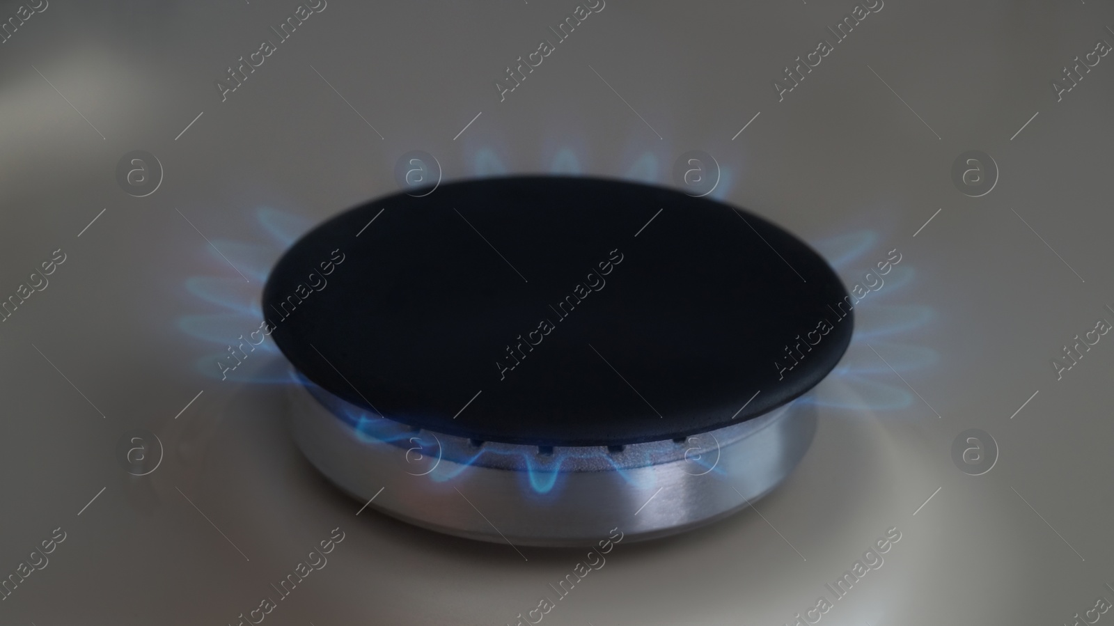 Photo of White gas cooktop with turned on burner, closeup