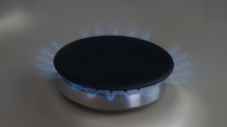 White gas cooktop with turned on burner, closeup