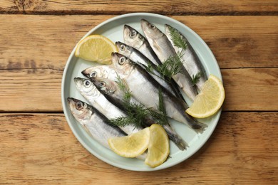 Fresh raw sprats, lemon and dill on wooden table, top view