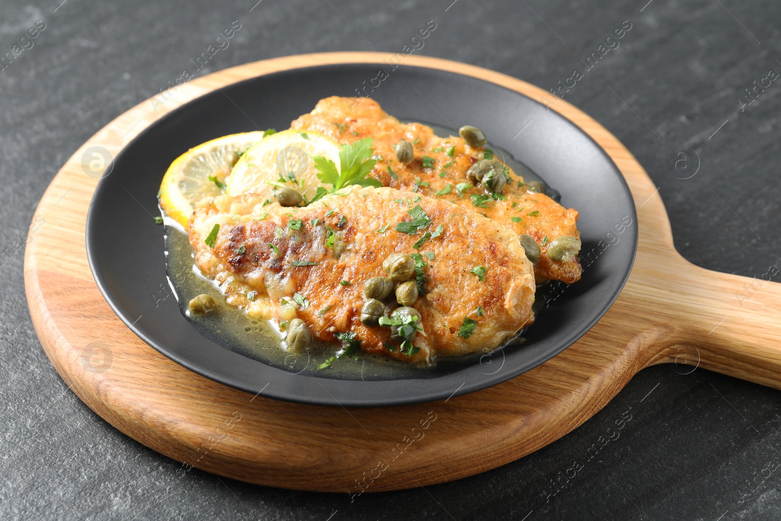 Photo of Delicious chicken piccata with herbs and lemons on black table