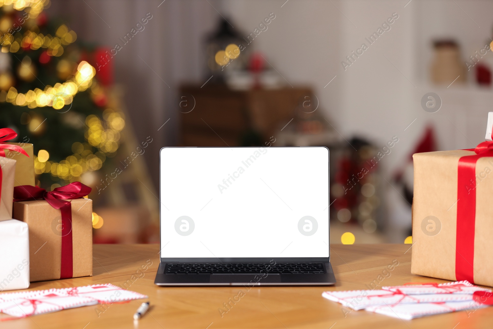 Photo of Laptop with blank screen, Christmas gifts and letters on table at home