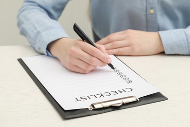 Photo of Woman filling Checklist at white wooden table, closeup