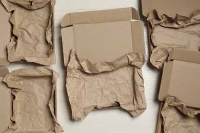 Many open cardboard boxes with crumpled paper on white wooden floor, flat lay