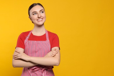 Beautiful young woman in clean striped apron on orange background. Space for text