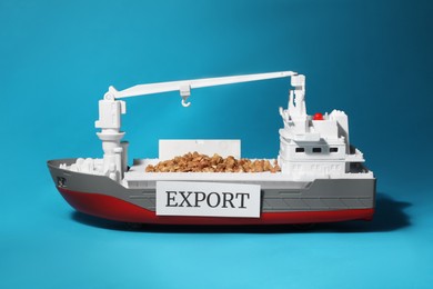 Photo of Toy cargo vessel with grains on light blue background. Export concept