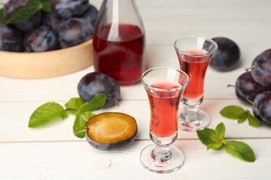 Photo of Delicious plum liquor, ripe fruits and mint on white wooden table. Homemade strong alcoholic beverage